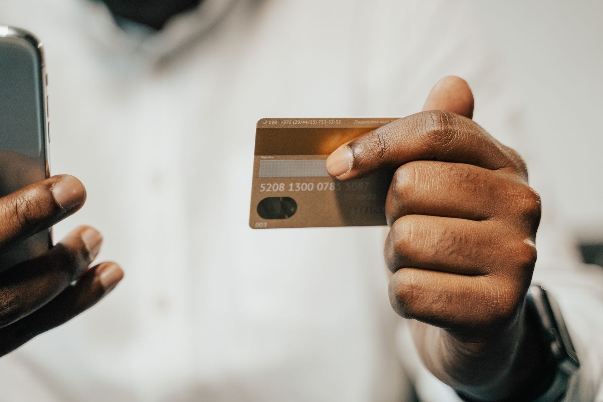 A person's hand holding a bank card next to a smartphone