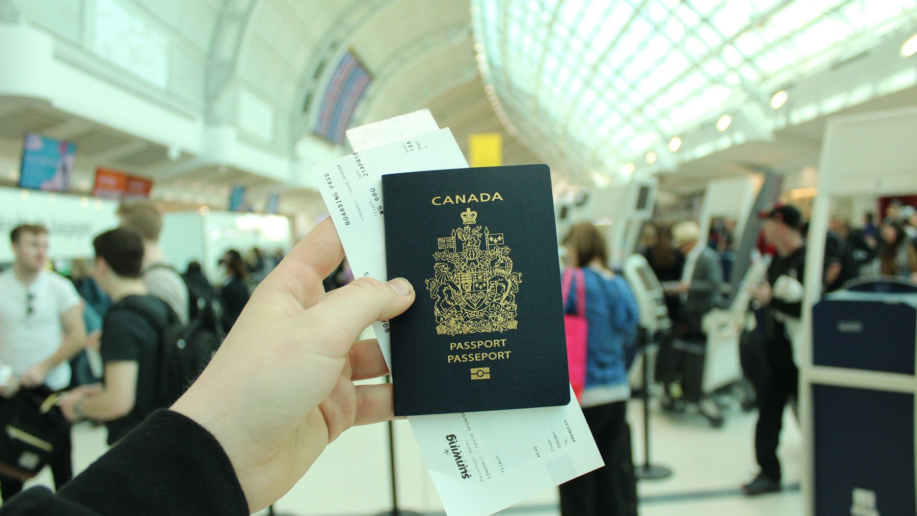 A hand holding a Canadian passport and boarding pass at the airport, ready to depart for Costa Rica