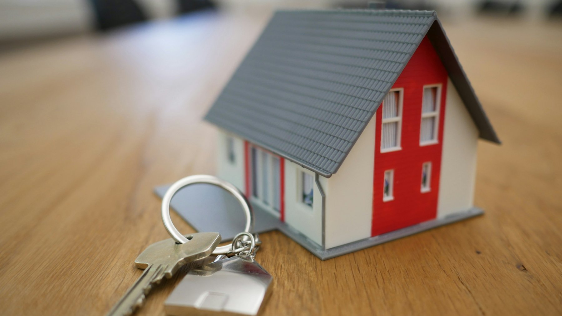 A small model house and a set of keys resting on a wooden table