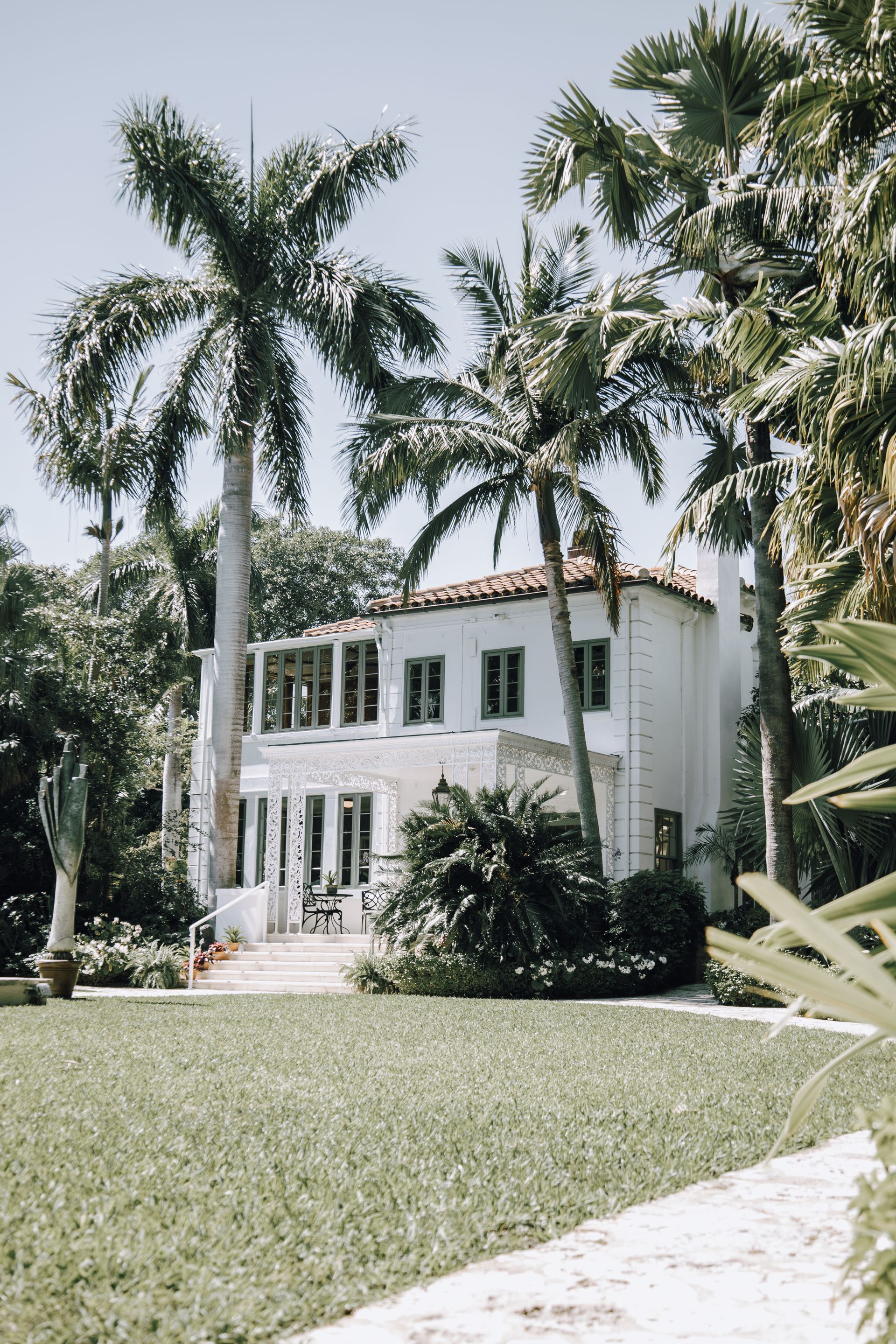 An elegant white two-story home with palm trees and a manicured lawn